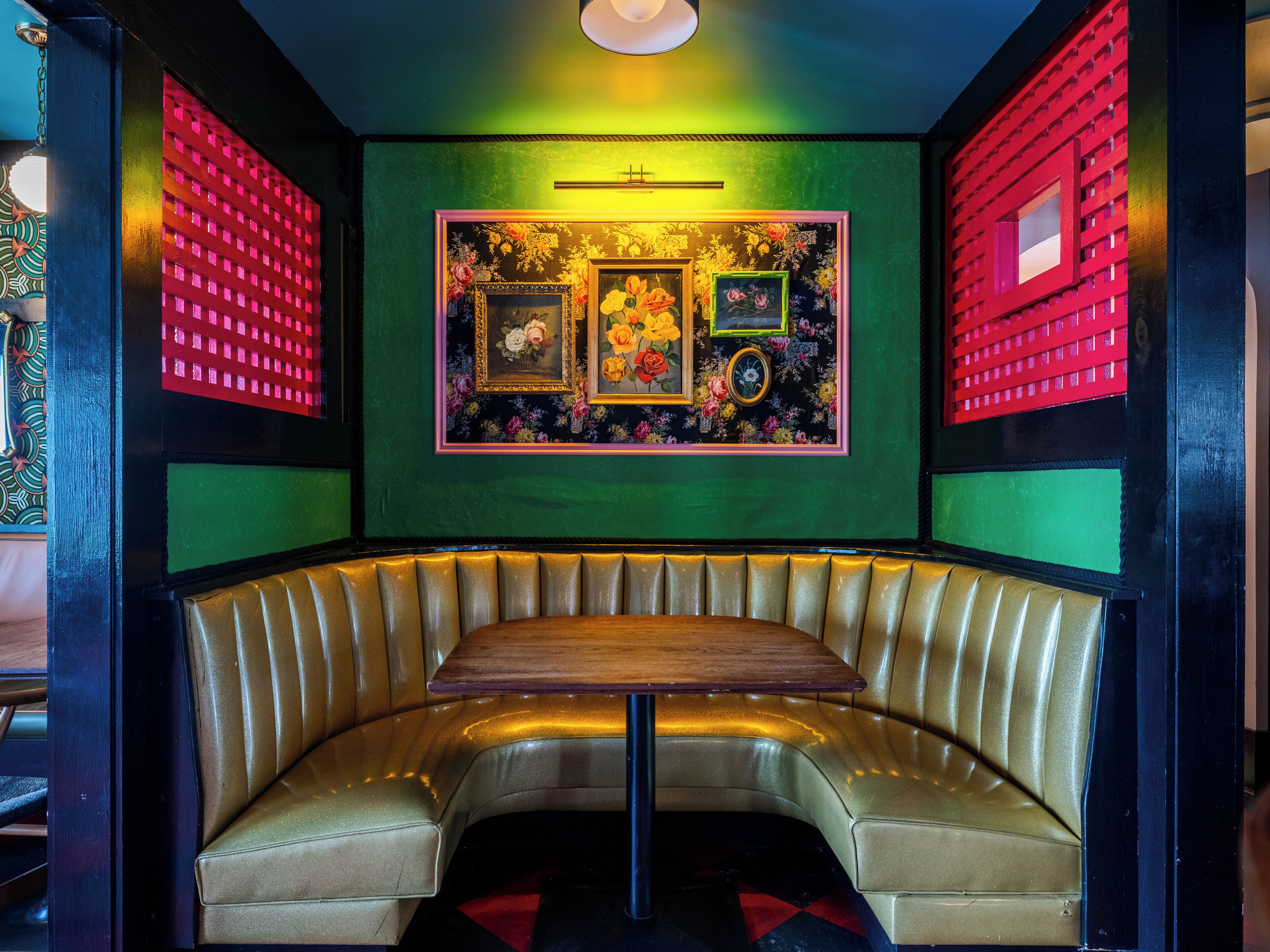 A booth with a wooden table and cushioned seating, surrounded by green walls with floral wallpaper and red decorative panels.