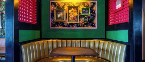 A booth with a wooden table and cushioned seating, surrounded by green walls with floral wallpaper and red decorative panels.