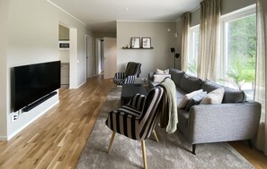 A modern living room with a flat-screen TV, a grey sofa, striped armchairs, and a coffee table.