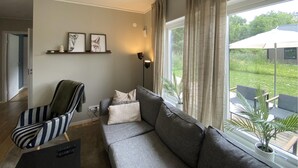 Un salon avec un canapé gris, un fauteuil à rayures et une étagère murale ornée de tableaux encadrés.
