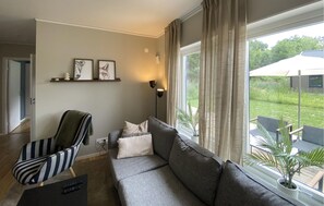 Ein Wohnzimmer mit grauem Sofa, Sesseln in Streifenmuster und einem Wandregal mit gerahmten Bildern.