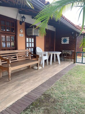 A wooden bench and a table with chairs outside a building with a tiled roof and a palm tree. - CASA DE PRAIA EM GERIBÁ (Búzios)