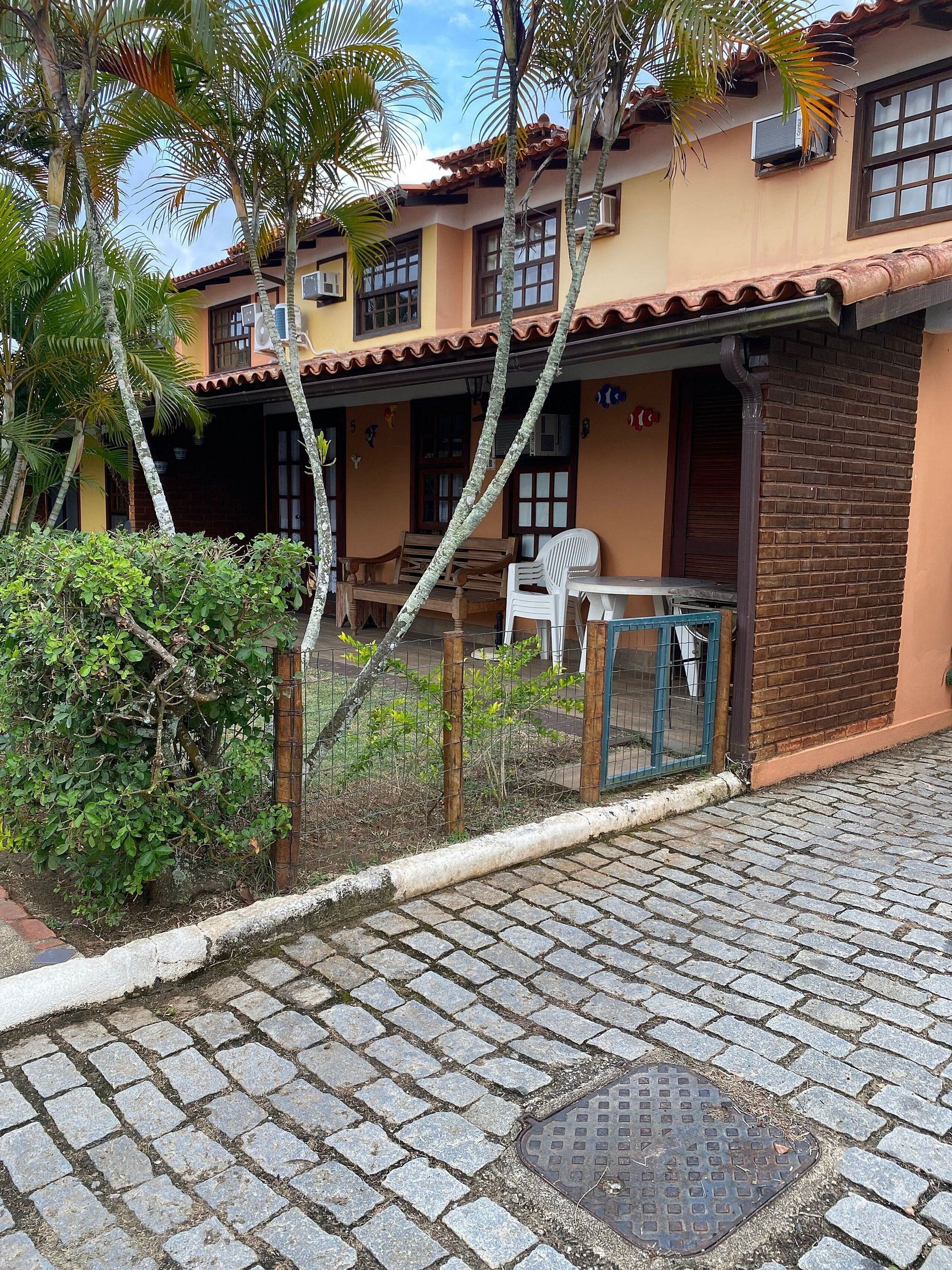 Un edificio de dos pisos con techo de tejas, pared de ladrillo y un patio cubierto con mesa y sillas.