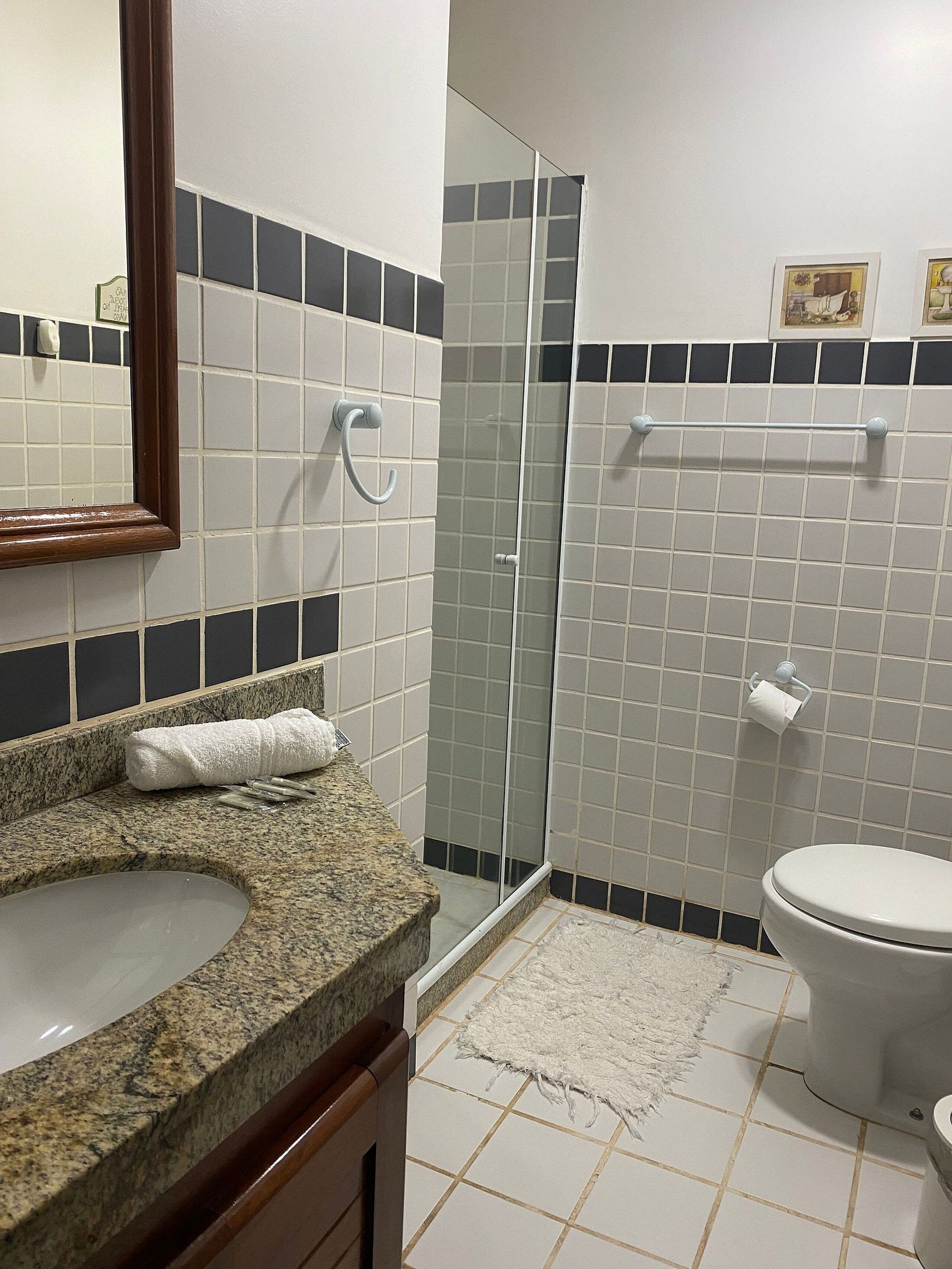 A bathroom with a granite countertop, a white sink, a glass shower enclosure, and a toilet.