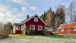 Una casa di legno rossa con tetto spiovente, un camino e un piccolo portico.