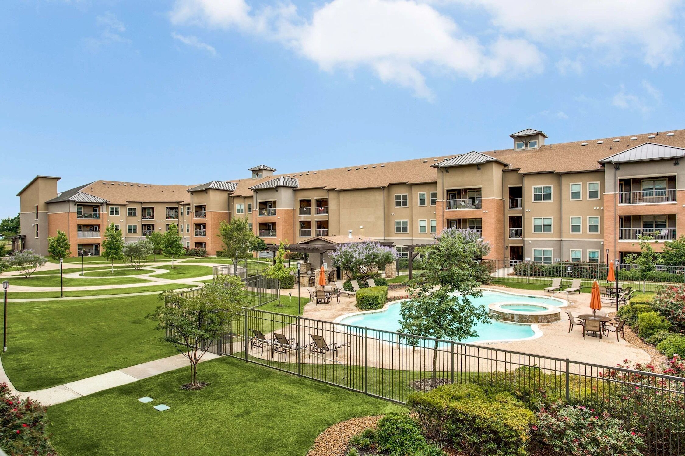 A multi-story hotel with a swimming pool, outdoor seating, and a landscaped garden.