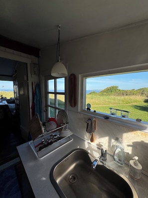 Una cocina con un lavaplatos de acero inoxidable, un escurreplatos y un ventanal con vista al mar.