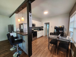 A modern kitchen with a bar area, wooden flooring, and a dining table with chairs.