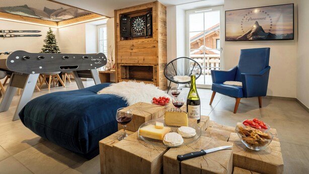 Une chambre moderne avec un lit, une table en bois sur laquelle se trouvent de la nourriture et des boissons, une chaise bleue, une cheminée et un porte-skis.