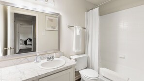 A bathroom with a marble sink, a toilet, and a shower with a curtain. - Landing Apartments near Southridge (Denton)
