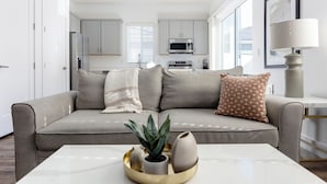 Un salon moderne avec un canapé gris, une table basse agrémentée d’objets décoratifs et une cuisine en arrière-plan.