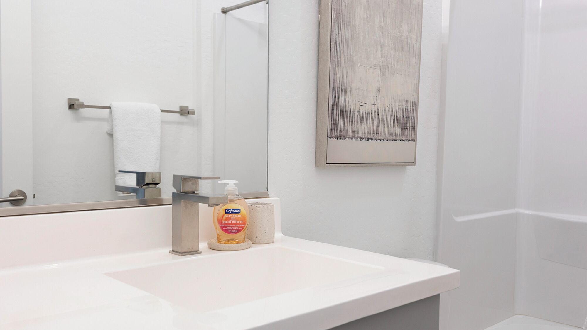 A bathroom with a white sink, a mirror, a towel rack, a soap dispenser, and a framed artwork on the wall.
