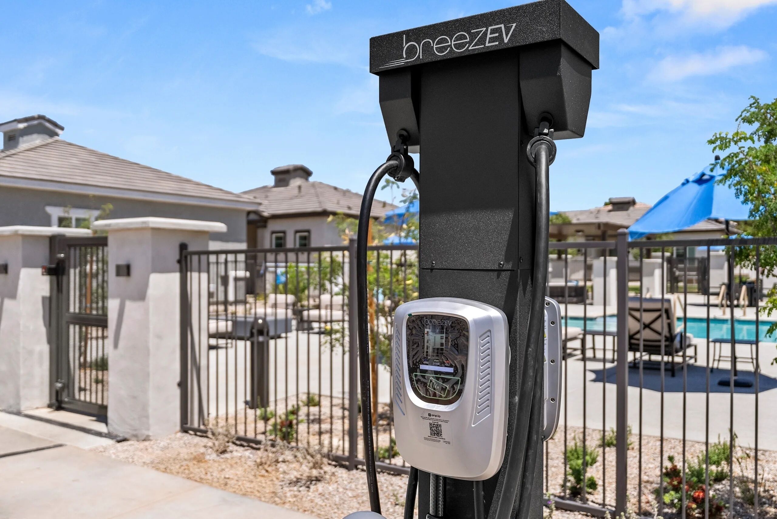 A BreezEV charging station with a clear view of a gated residential area, including a swimming pool and outdoor furniture.