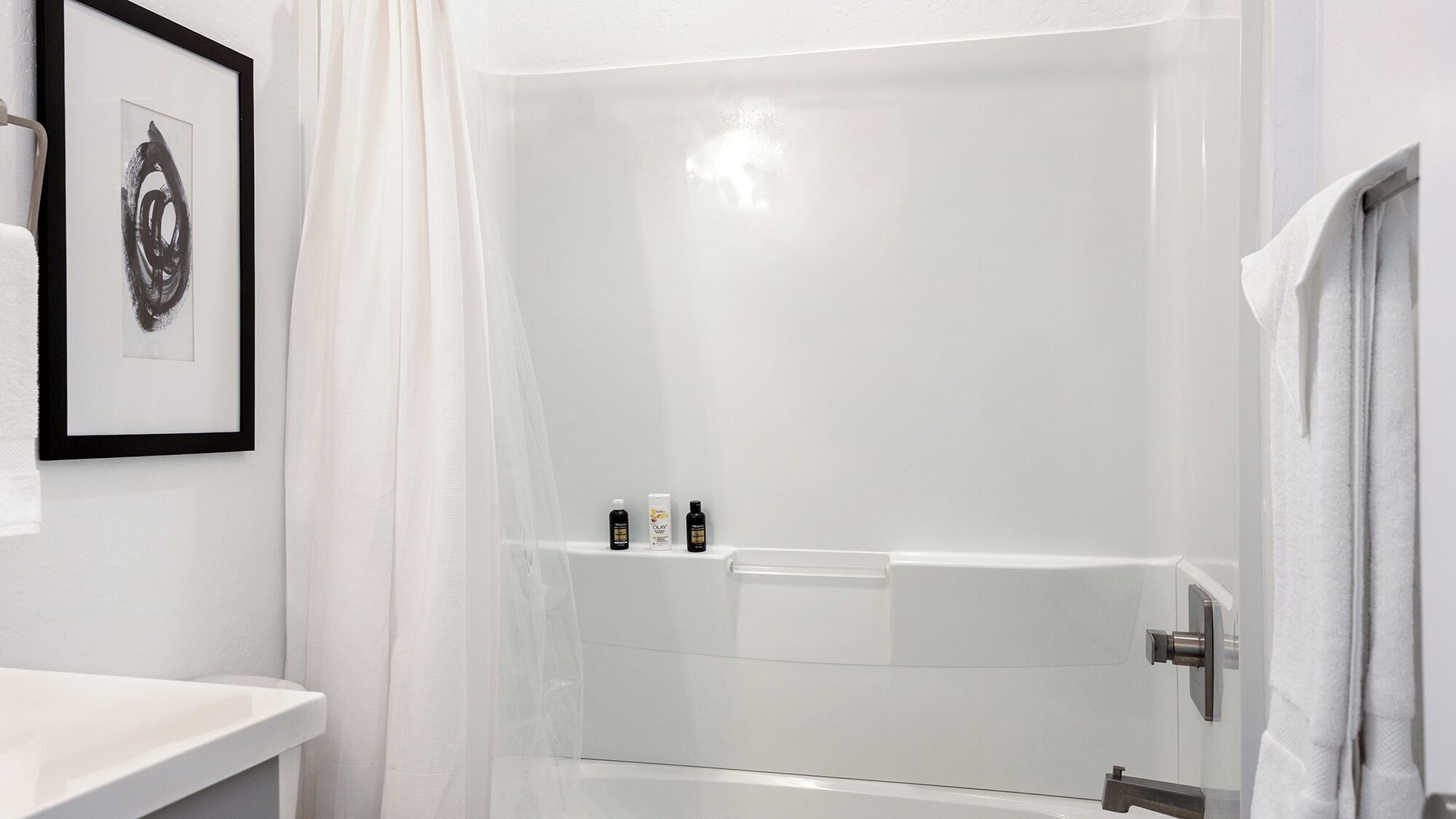 A modern bathroom with a glass-enclosed shower, a white sink, and a framed artwork on the wall.