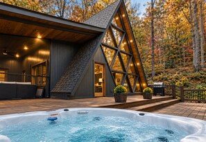Ein modernes Blockhaus mit Whirlpool, einer Holzterrasse und einem großen Fenster mit Blick auf einen Wald.