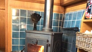 A wood-burning stove with a chimney, a metal bucket, and a woven basket on a tiled floor.