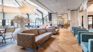 A spacious lobby with a wooden floor, a large white vase with branches, and seating areas with sofas and armchairs. - Tiny House Near North Sea Beach (Kamperland)