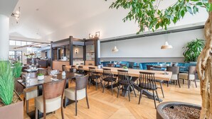 A modern restaurant with wooden tables and chairs, a bar area, and a seating section with blue cushioned benches. - Tiny House Near North Sea Beach (Kamperland)