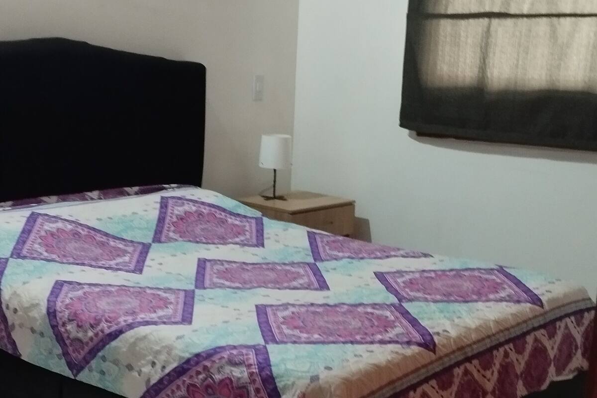 A bedroom with a bed, a nightstand, a lamp, and a window with curtains.