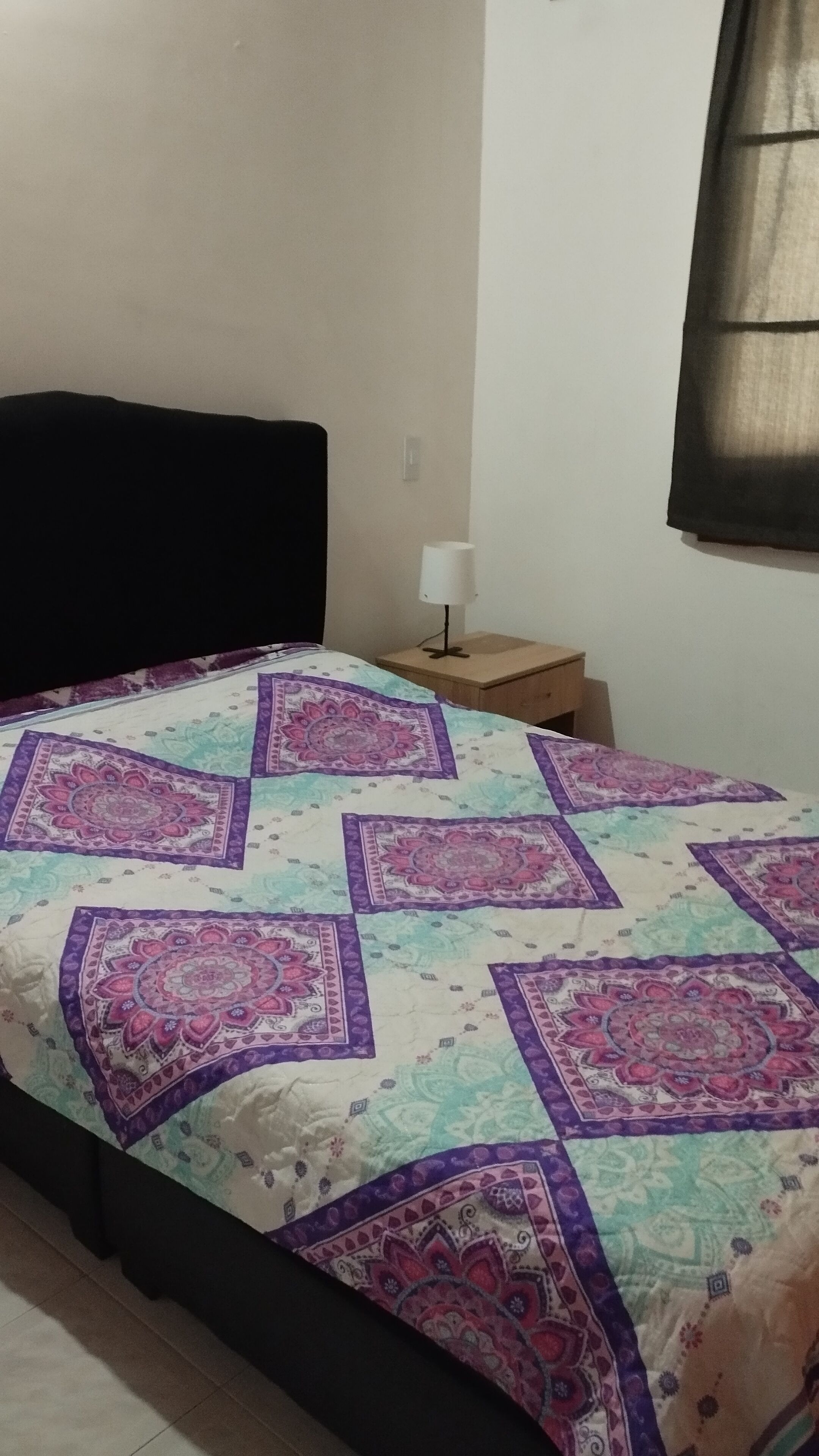 A bedroom with a bed, a nightstand, a lamp, and a window with curtains.