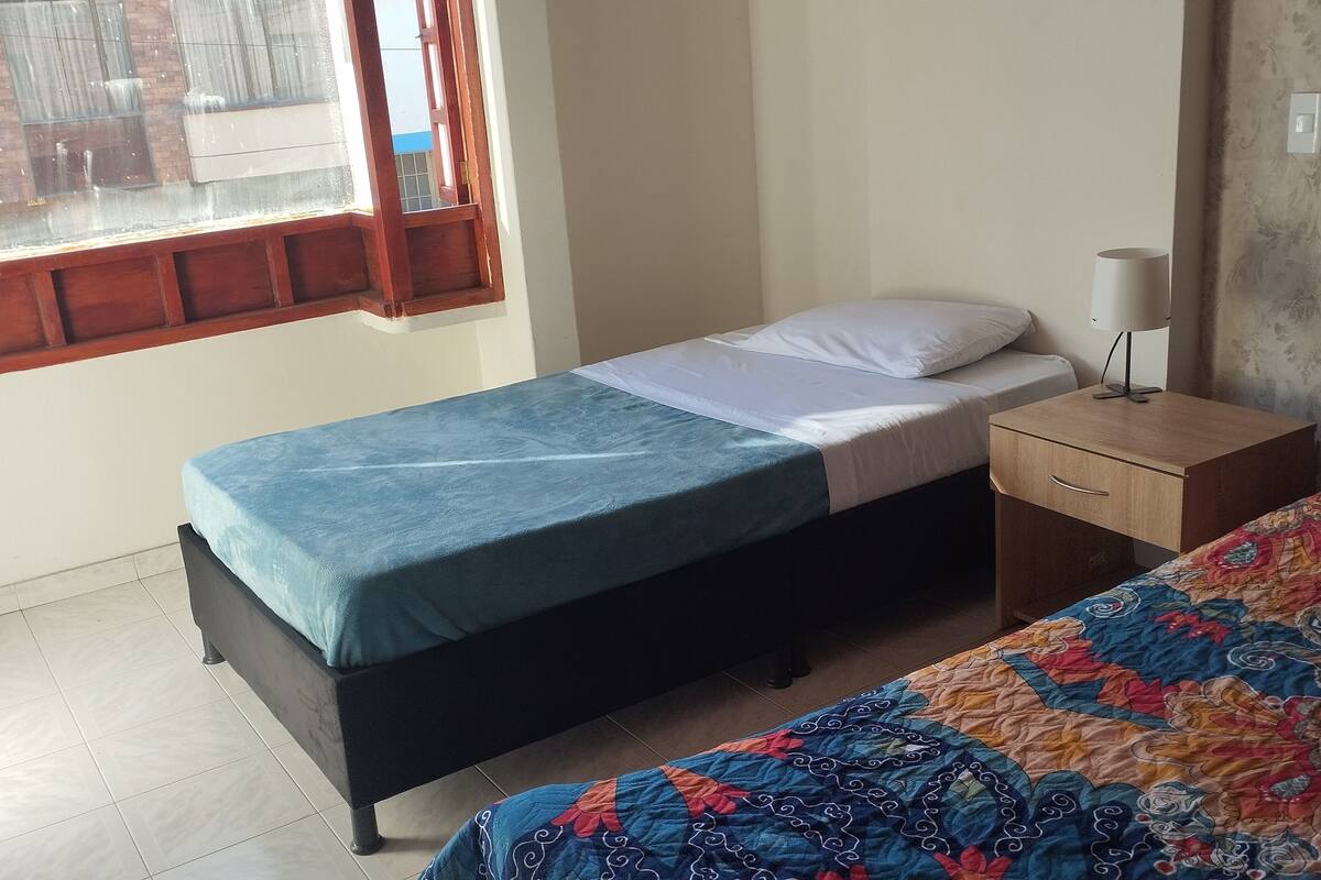 A bedroom with a single bed, a bedside table with a lamp, and a window with curtains.