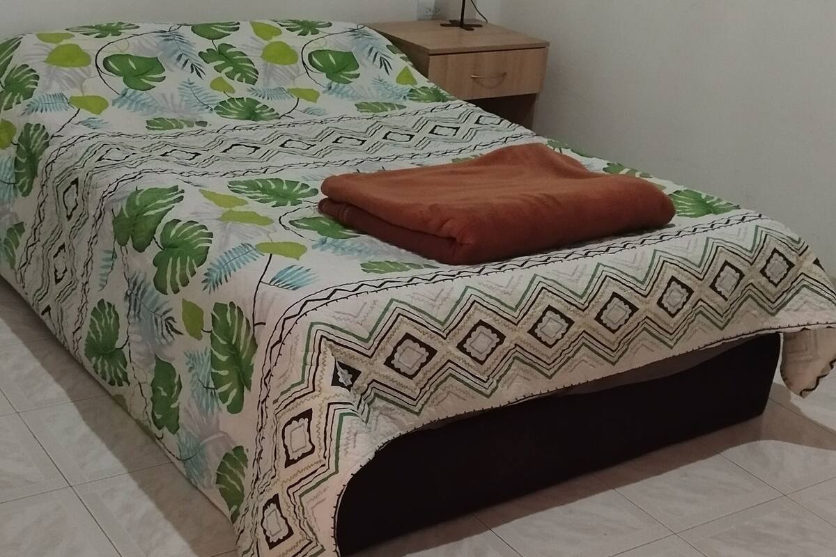A bed with a patterned bedspread, a brown pillow, and a nightstand with a lamp.