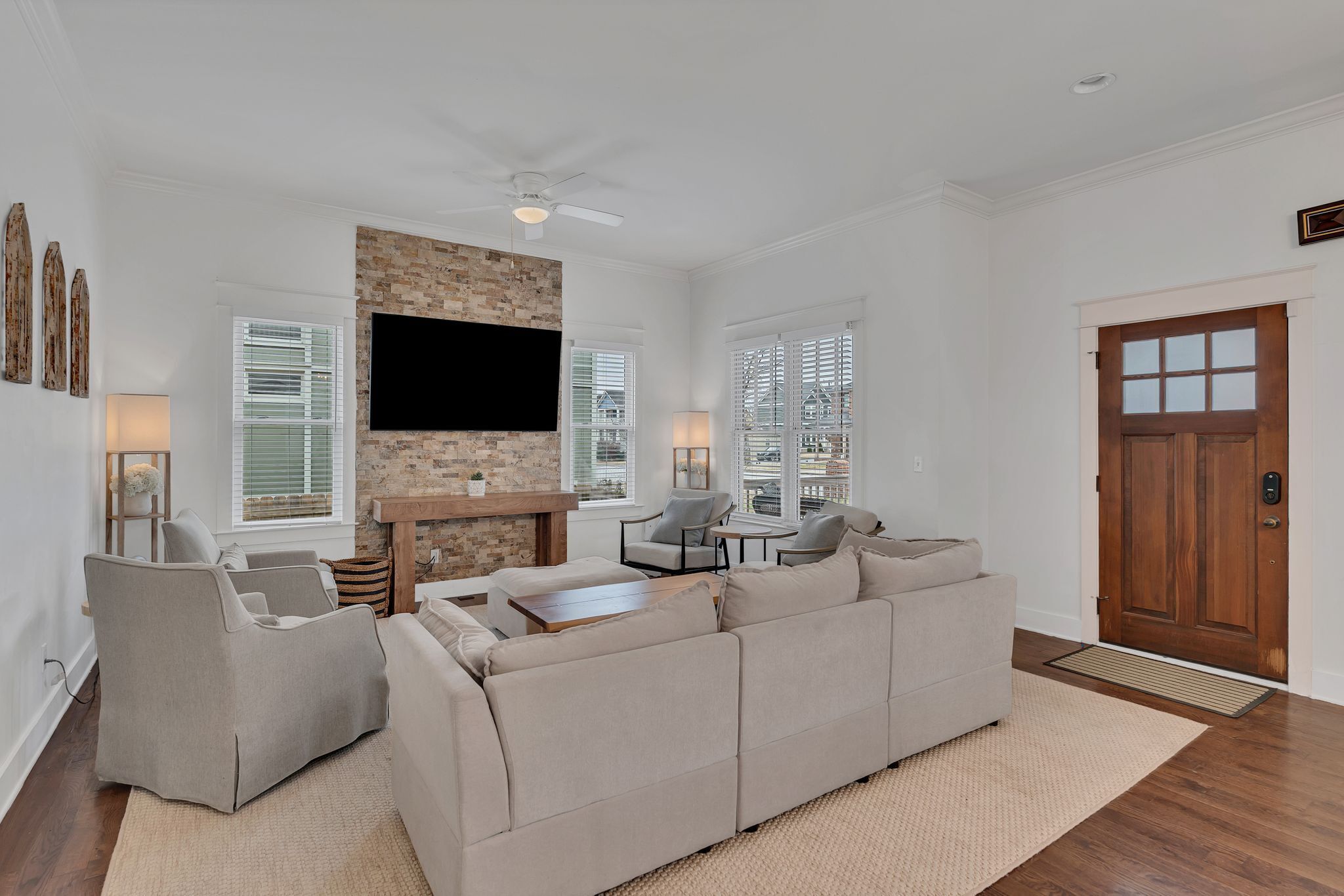 A living room with a beige sofa, two armchairs, a fireplace, a flat-screen TV, and a wooden door.