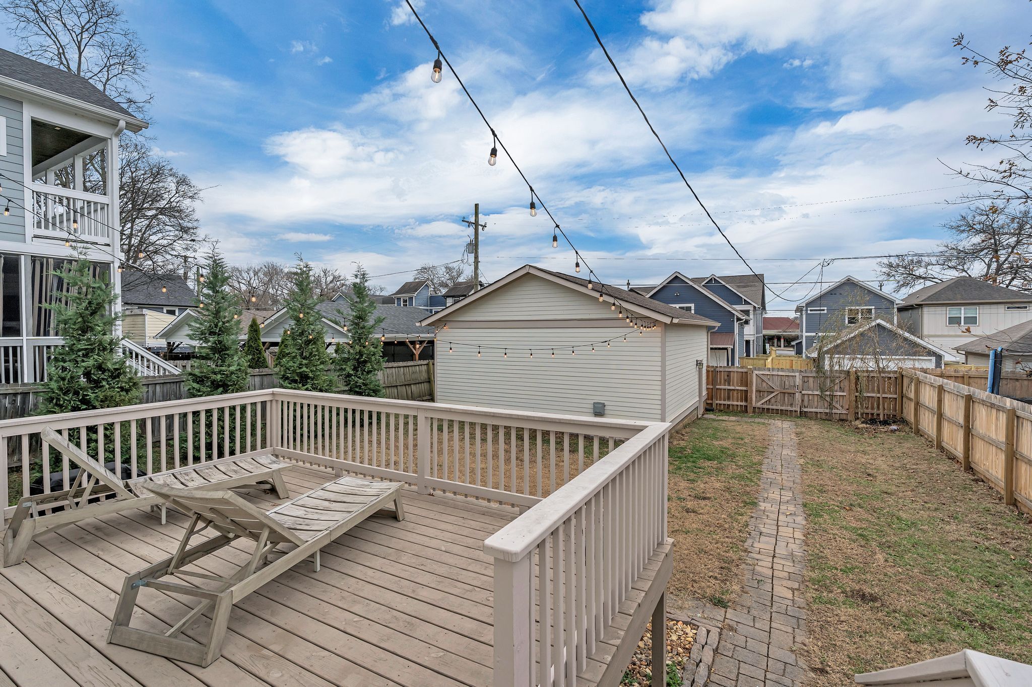 A wooden deck with a built-in bench, a small shed, and a brick pathway leading to a wooden fence.