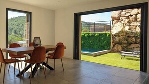Un comedor moderno con mesa y sillas, grandes ventanales que ofrecen vistas a un muro de piedra y follaje.
