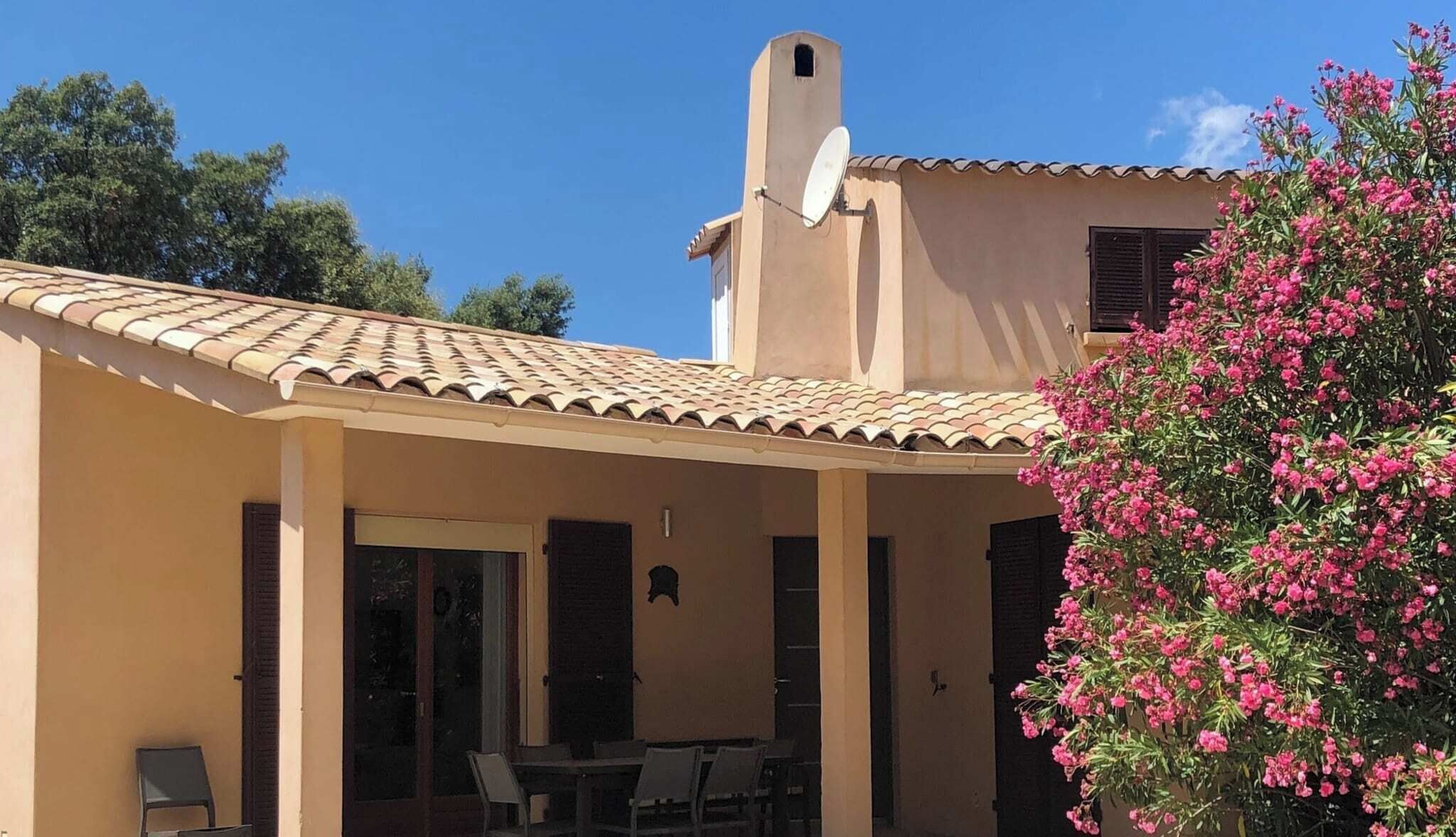 A building with a tiled roof, a satellite dish, and a covered patio area with chairs and a table.