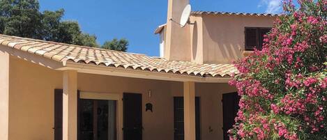A building with a tiled roof, a satellite dish, and a covered patio area with chairs and a table.