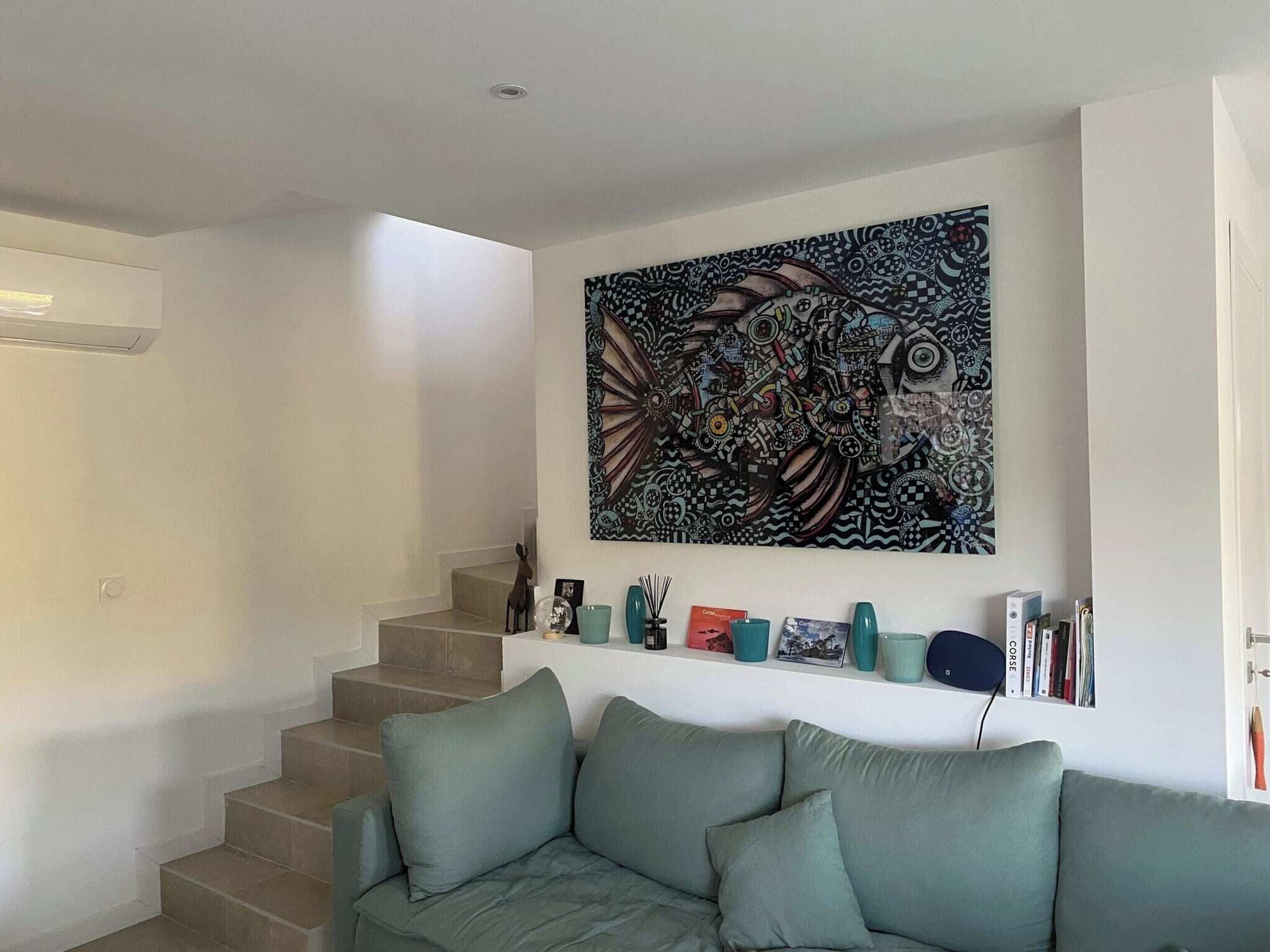 Una sala de estar con una escalera, un sofá verde y un cuadro abstracto grande en la pared.