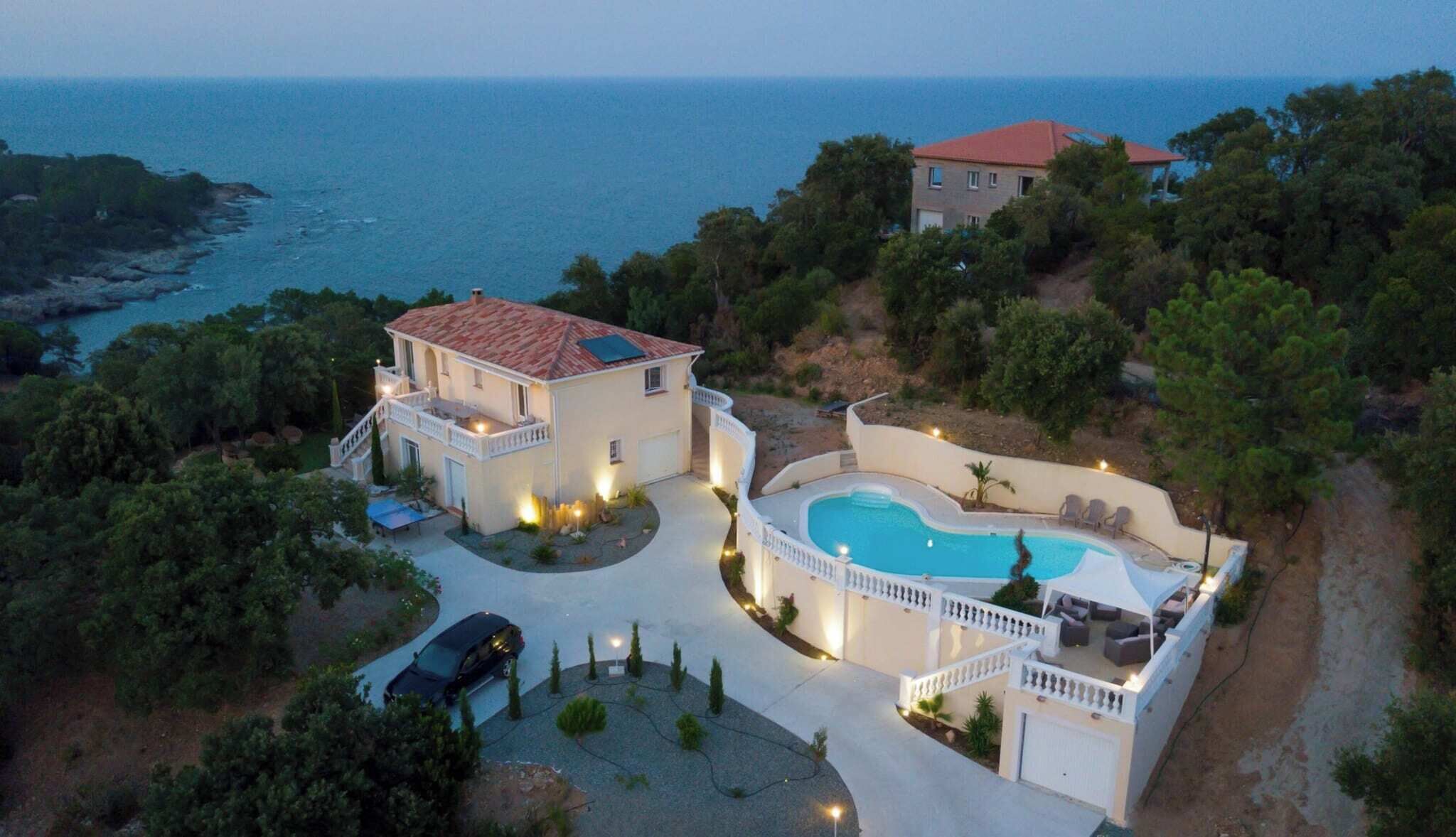 Uma casa de dois andares com piscina, cercada por árvores e com vista para o mar.