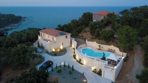 Una casa de dos pisos con piscina, rodeada de árboles y con vista al mar.