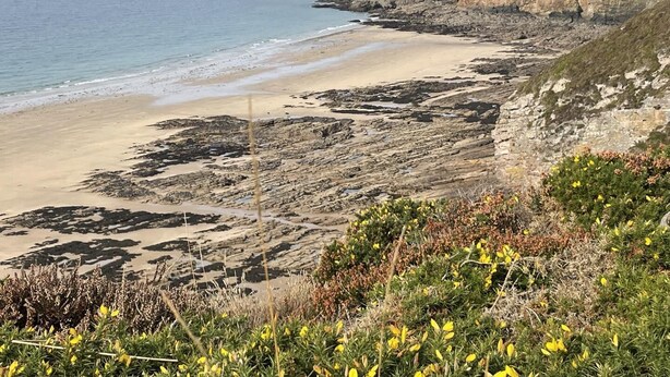 Eine Küstenlandschaft mit Sandstrand, Felsenküste und einem Leuchtturm in der Ferne.