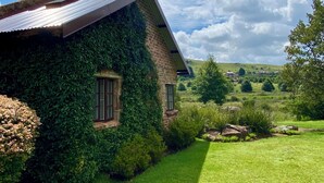 A house with ivy-covered walls and a sloped roof, surrounded by a well-maintained lawn and a scenic countryside view.