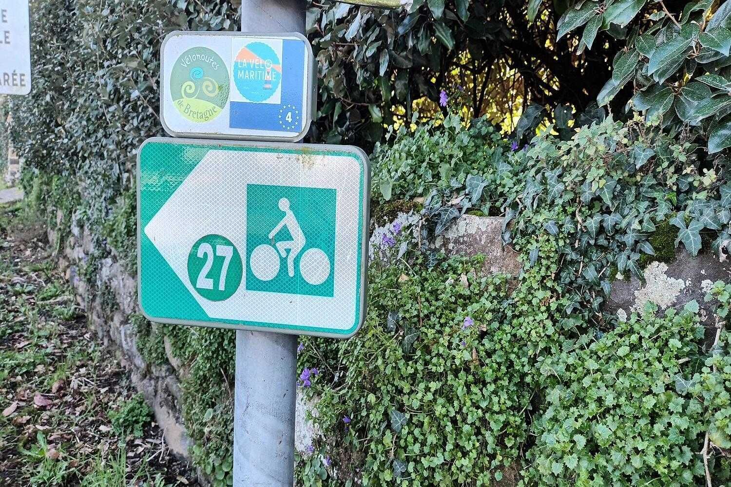Un panneau de signalisation indiquant la direction à suivre, avec un symbole de vélo et le numéro 27, ce qui signale une piste cyclable.