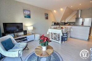 A modern living room with a flat-screen TV, a sofa, a coffee table, and a dining area with a table and chairs. - Le Balcon de la Baie (PAIMPOL)