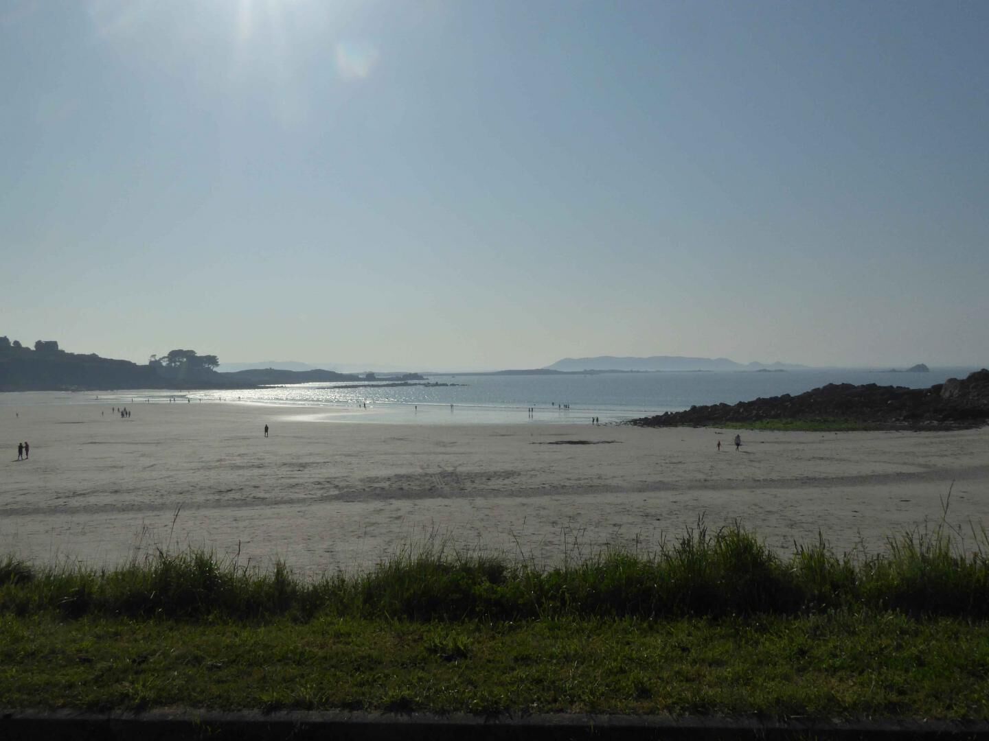 A beach with a clear sky, calm sea, and distant mountains.