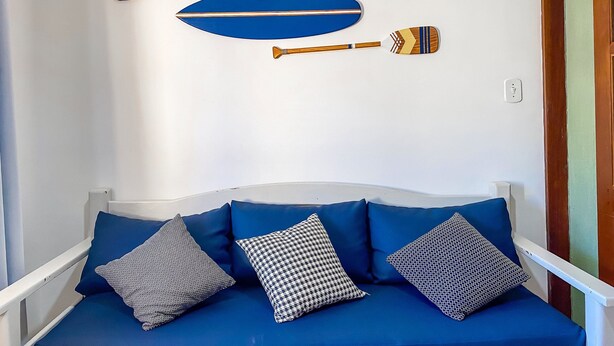 A blue sofa with patterned cushions, a white wall, and two wooden paddles mounted on the wall. - Condomíno American Praia  (Porto Seguro)