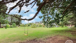 Une cour verdoyante avec une balançoire, entourée d’arbres et avec un bâtiment en arrière-plan.