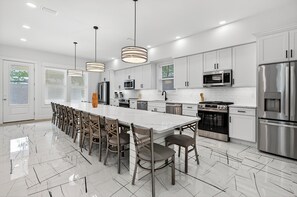 A modern kitchen with white cabinets, stainless steel appliances, and a large island with seating. - The Grand 30A - Luxury Home in 30A Suitable for Beach Retreats & Large Groups (Santa Rosa Beach)