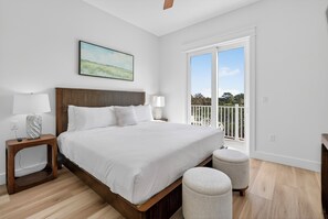 A bedroom with a large bed, a nightstand, a lamp, a small ottoman, and a balcony with a view. - Seaside Reunion  - Luxury Home in 30A Perfect for Beach Retreats & Large Groups (Santa Rosa Beach)