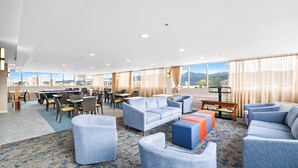 Un'ampia hall dell'hotel con tavolo da biliardo, diverse zone relax e grandi finestre che offrono vista sulla città.