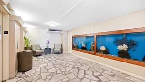 Una hall con pavimento in pietra, due poltrone, una pianta in vaso e un grande acquario.