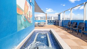 Una terrazza esterna illuminata dal sole con idromassaggio, poltrone relax e un murale.