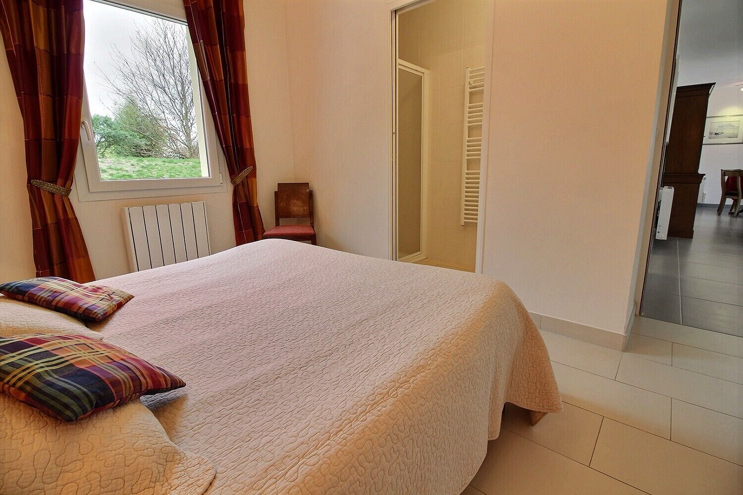 Ein Schlafzimmer mit Bett, einem fenster mit Vorhängen, einer Heizung und einer Tür zu einem Badezimmer.