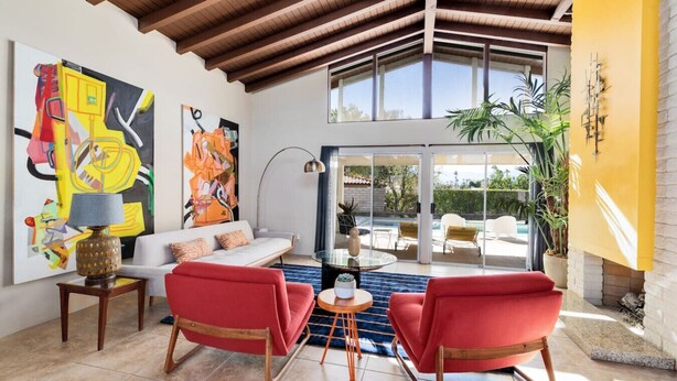 Ein modernes Wohnzimmer mit einem weißen Sofa, roten Sesseln, abstrakter Kunst und Blick auf einen Pool.