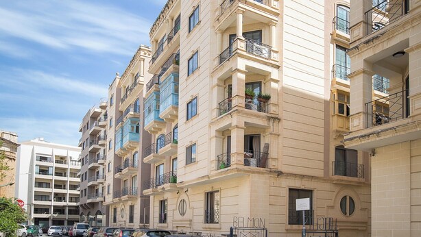 Ein mehrgeschossiges Wohnhaus mit Balkonen, geparkten Autos und blauem Himmel.