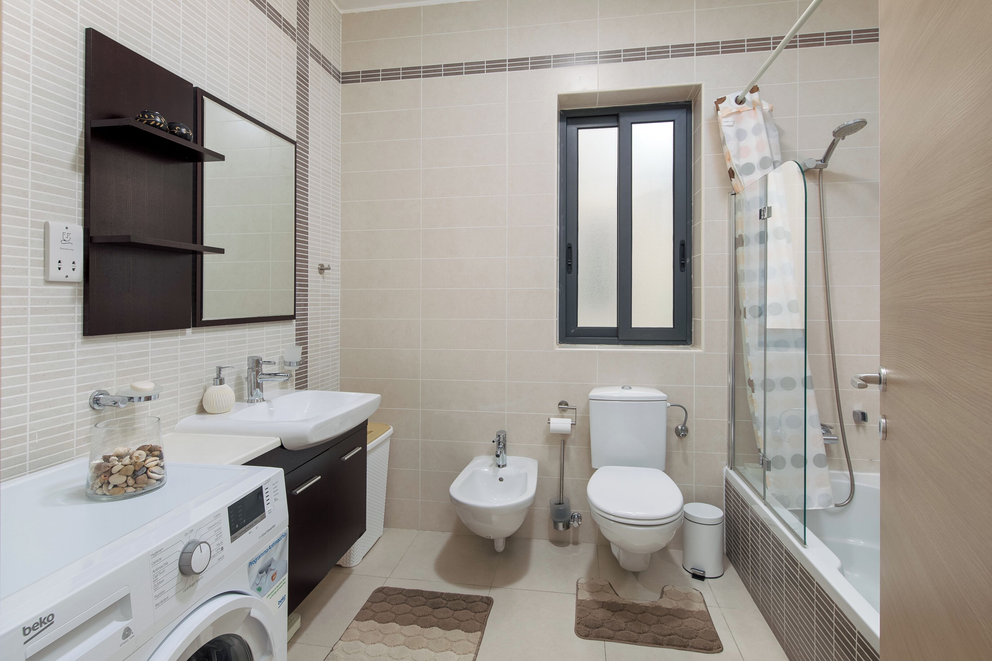 Een moderne badkamer met een wasmachine, bidet, toilet en douchecabine.